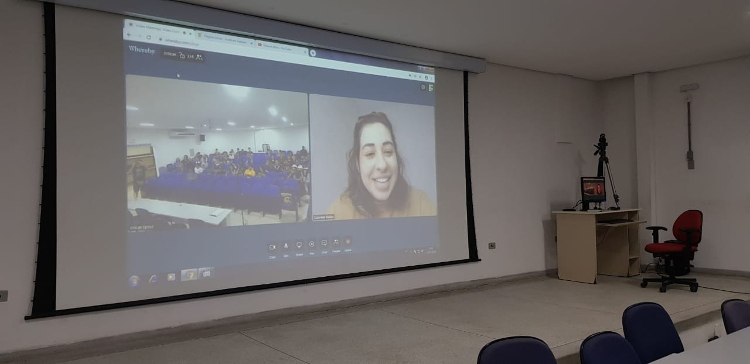 Foto Tela do auditório durante a videoconferência mostrando de um lado os alunos e do outro Gabriela Bailas